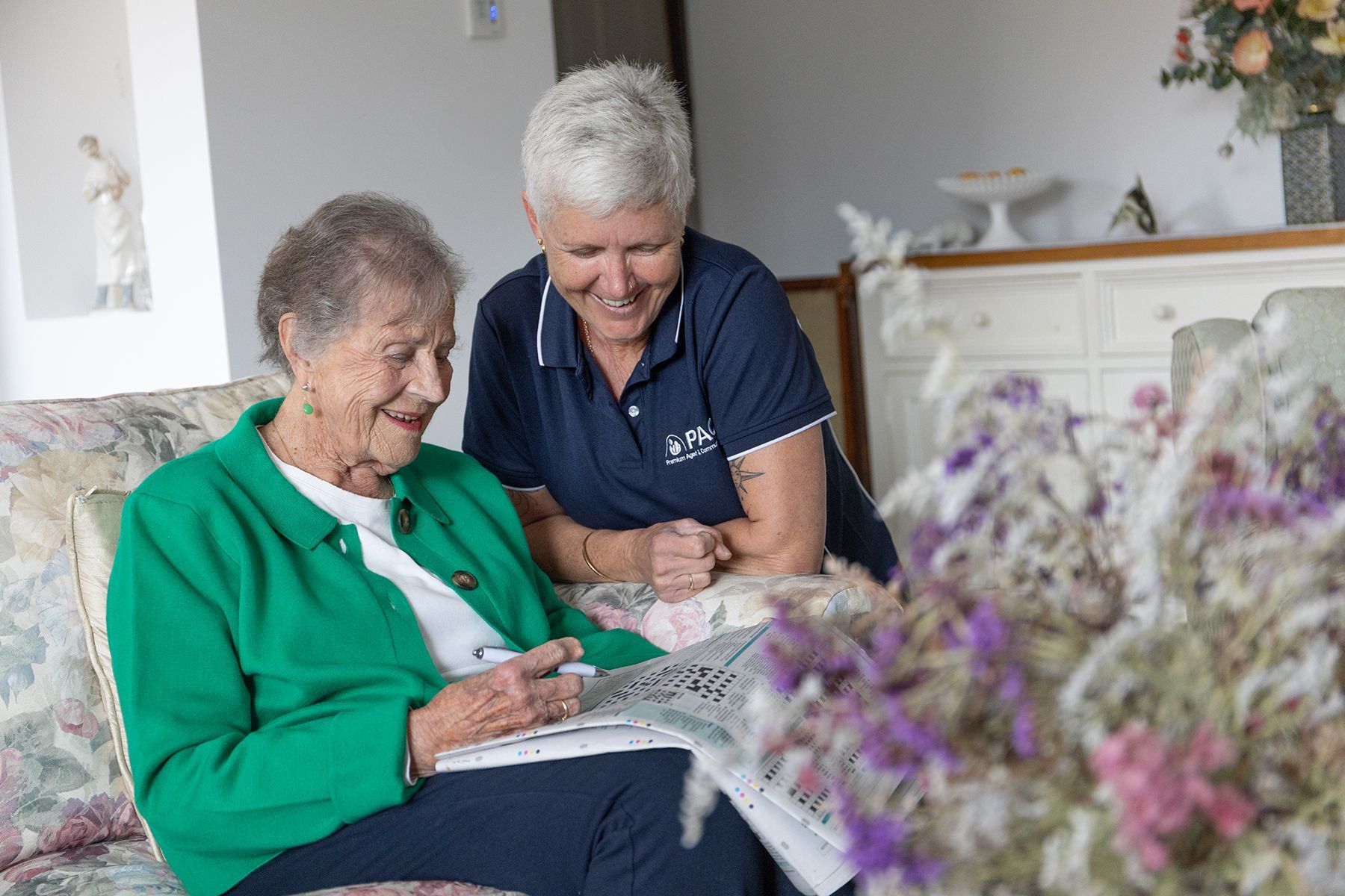 Woman in Green Jacket Doing Crossword With Caregiver — Premium Aged & Community Services In Armidale, NSW