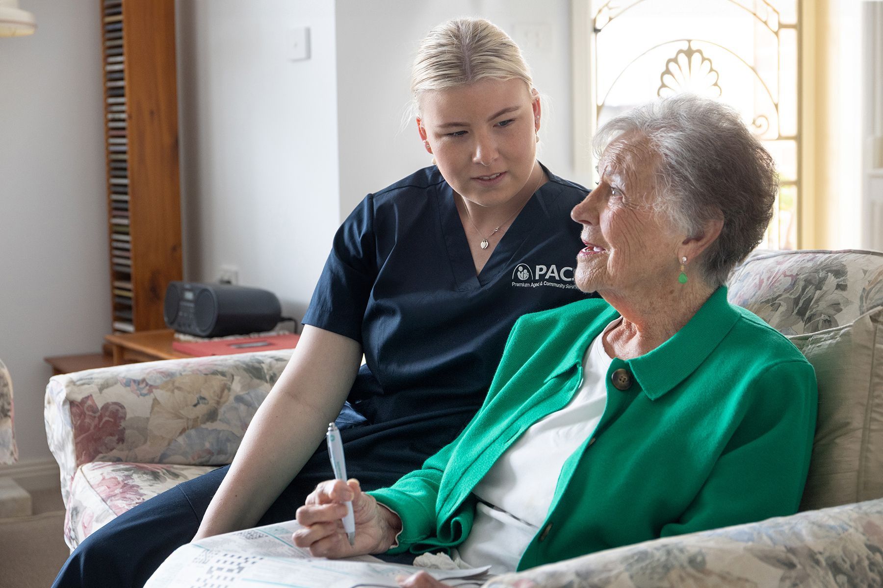 Caregiver in Navy Scrubs Talking to an Elderly Woman in a Green Jacket — Premium Aged & Community Services In Gunnedah, NSW