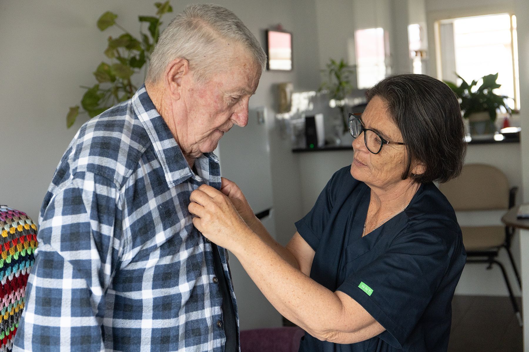 A Person in Scrubs Helps a Person in a Plaid Shirt Button — Premium Aged & Community Services In Moree, NSW