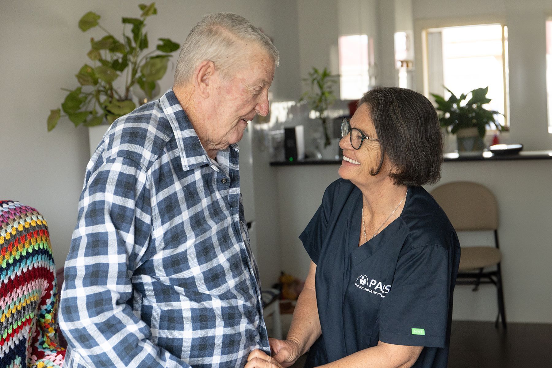 Person in Blue Plaid Shirt and Caregiver in Scrubs Smiling at Each Other — Premium Aged & Community Services In Tamworth, NSW