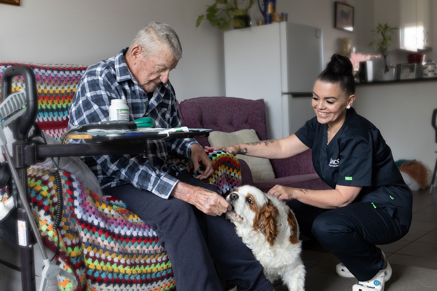Man Seated, Petting Dog, Assisted by Caregiver. Living Room Setting — Premium Aged & Community Services In Tamworth, NSW