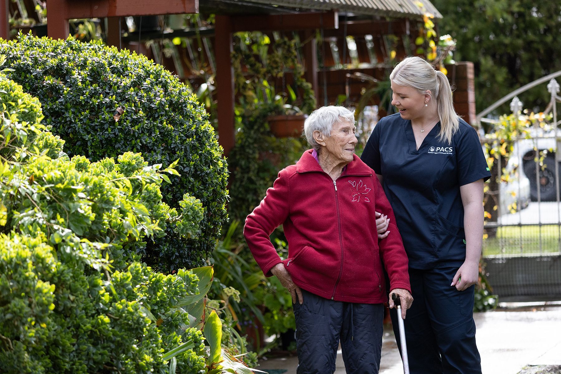 A Caregiver Assists an Older Person Walking Outdoors With a Cane — Premium Aged & Community Services In Tamworth, NSW