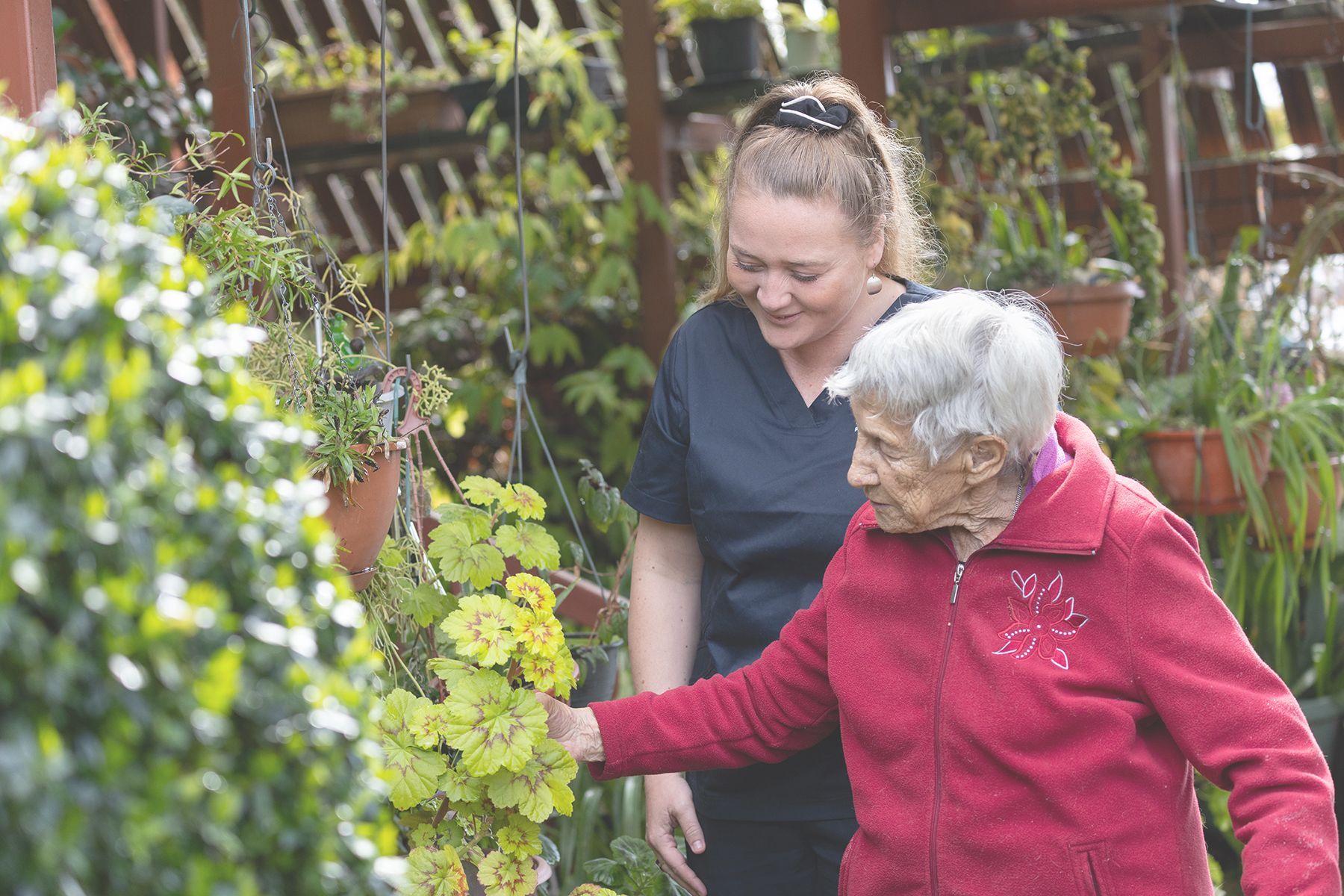Woman in Red Jacket and Caregiver Looking at Plants in a Garden — Premium Aged & Community Services In Armidale, NSW