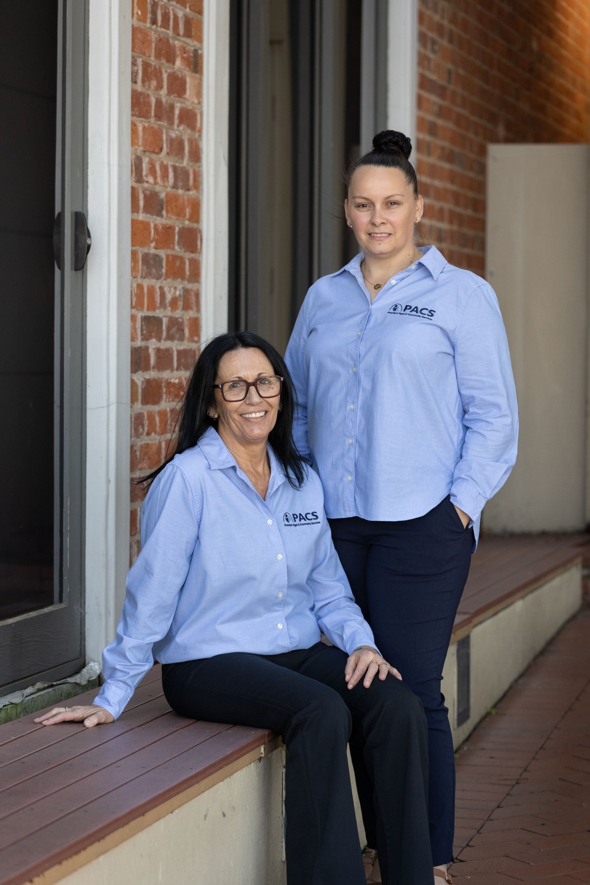 Two Women in Matching Blue Shirts Pose on a Porch — Premium Aged & Community Services In Tamworth, NSW
