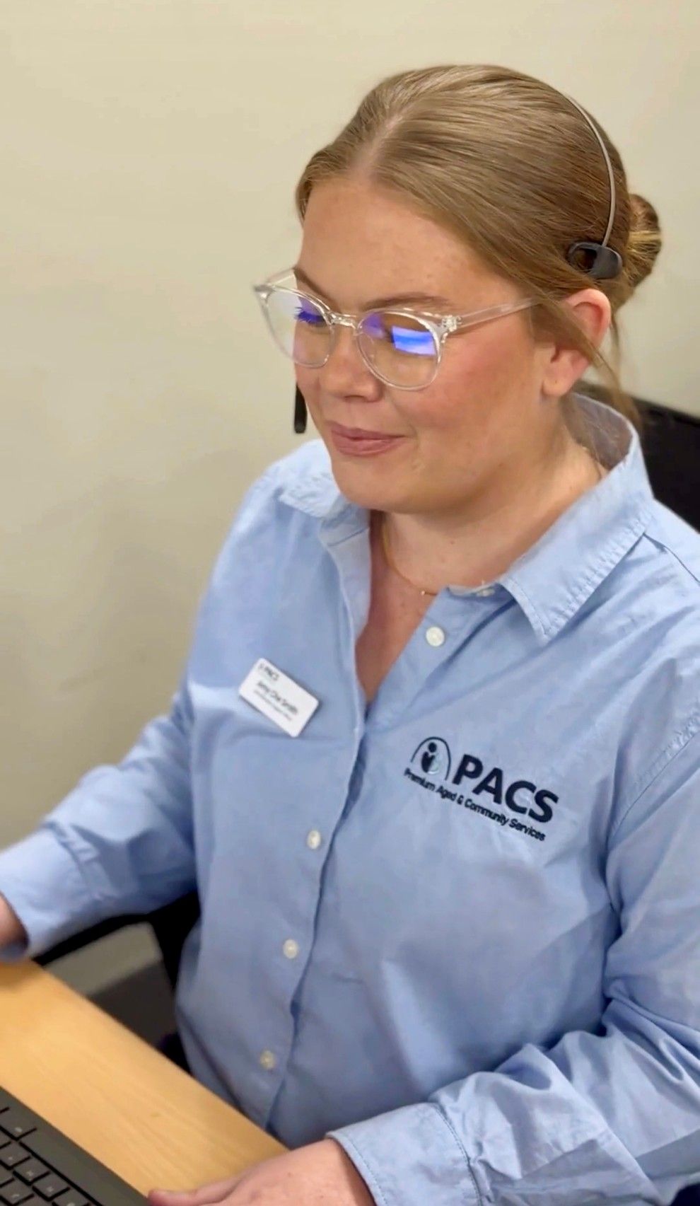 Woman Wearing Glasses and a Blue Pacs Uniform, Working at a Computer — Premium Aged & Community Services In Tamworth, NSW