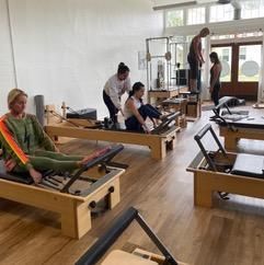 A group of people are sitting on pilates reformers in a studio.
