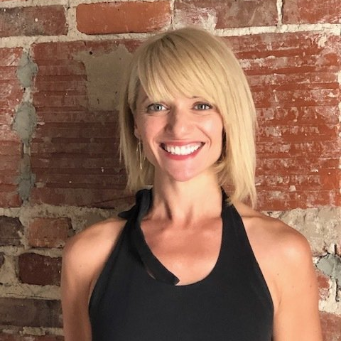 A woman in a black tank top is smiling in front of a brick wall