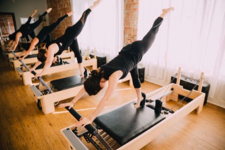 A group of women are doing pilates exercises on pilates machines in a gym.