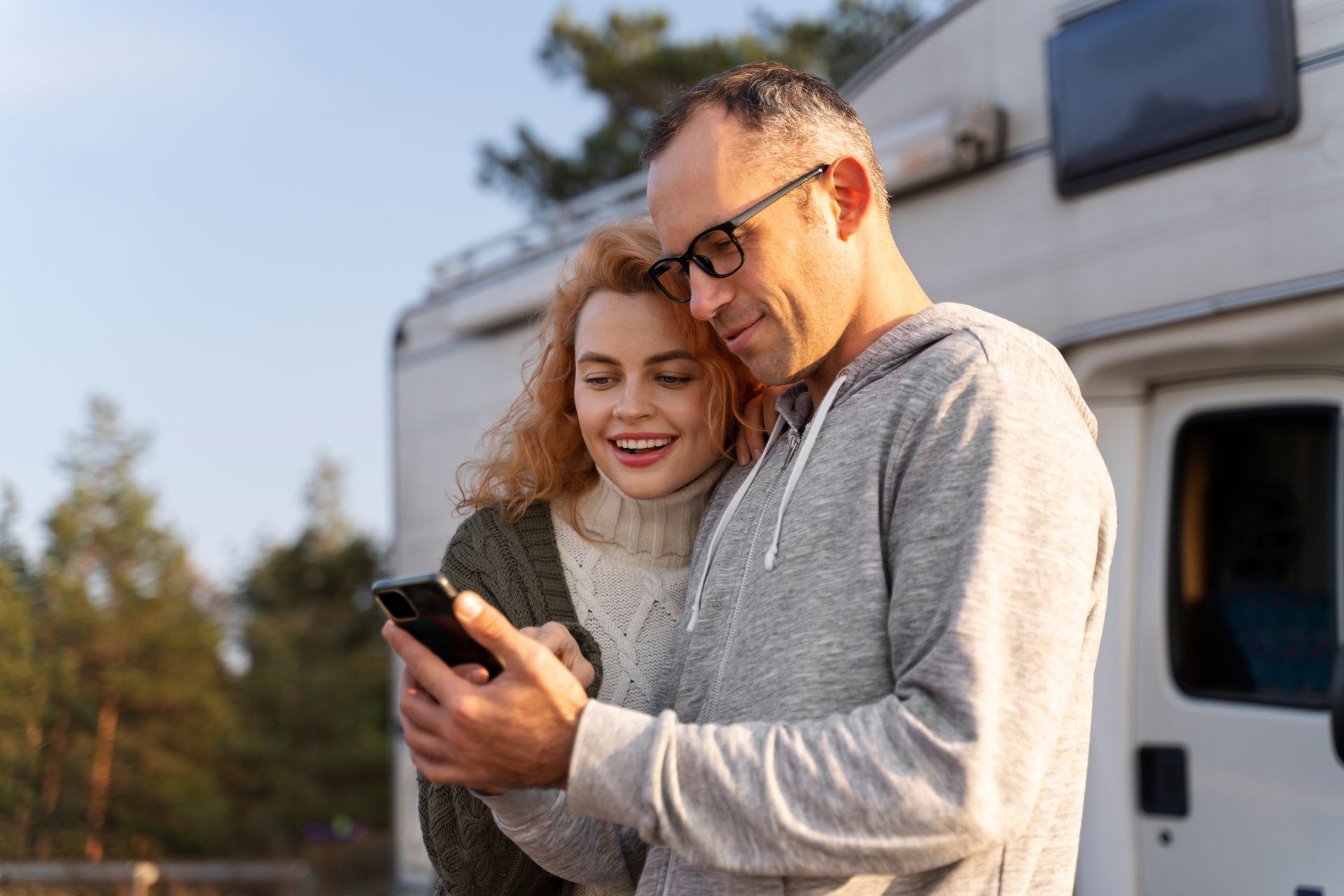 A man and a woman are looking at a cell phone in front of a camper van.