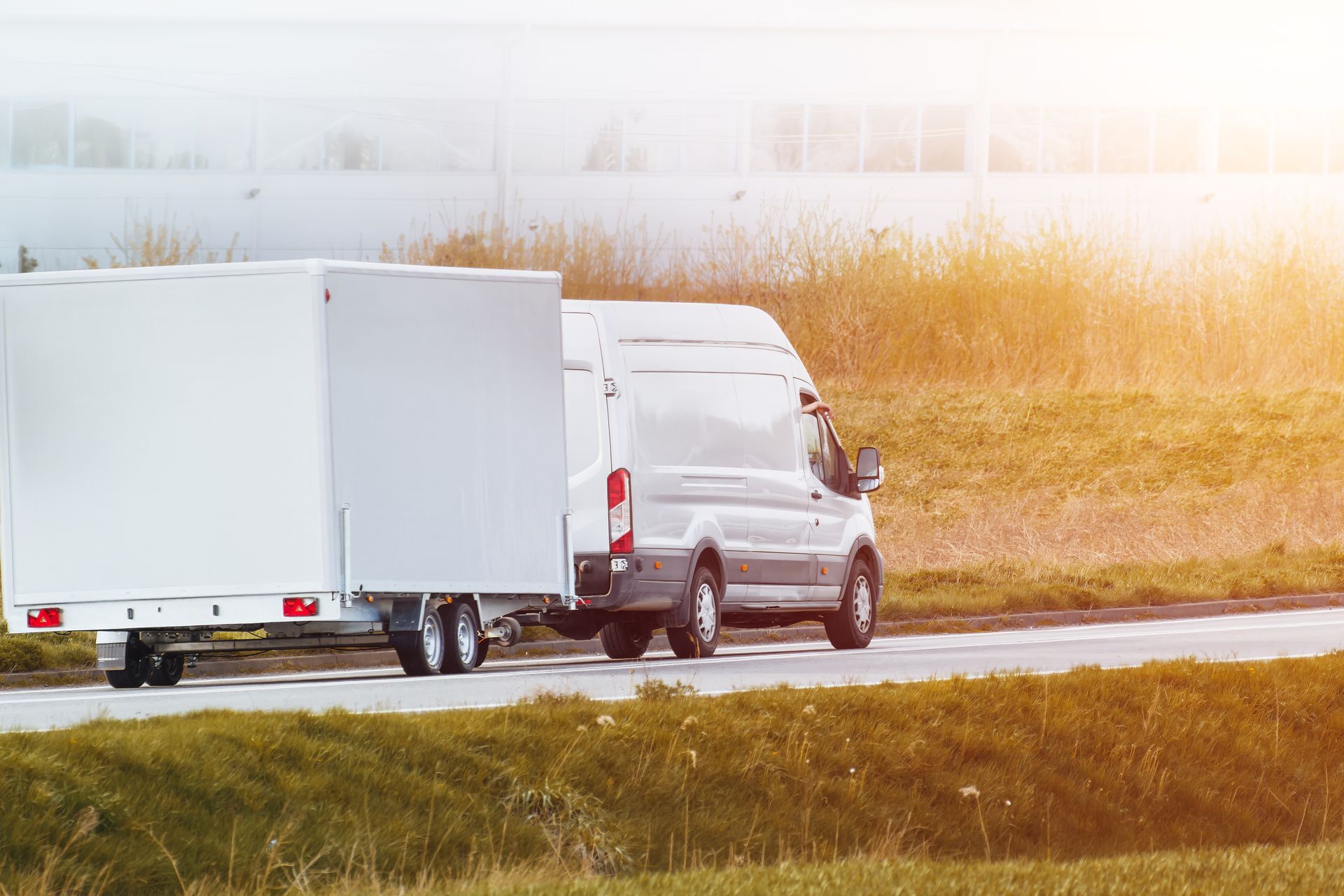 A white van is towing a trailer down a road.
