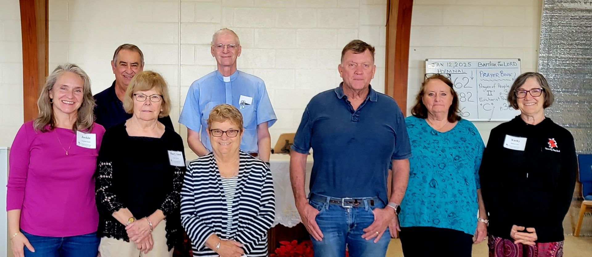 A group of nine people smiling for the camera, standing indoors.