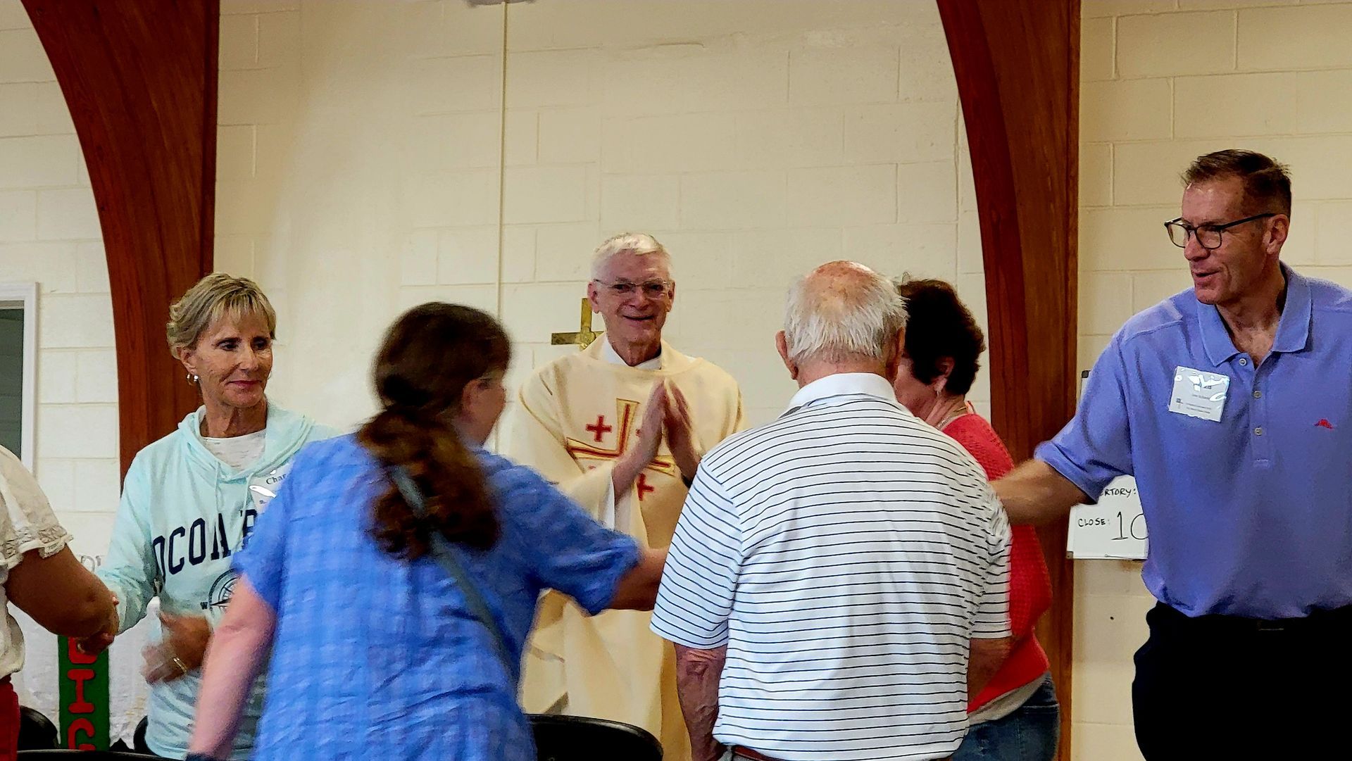 A group of people surrounding a priest, possibly a blessing or prayer in a church setting.