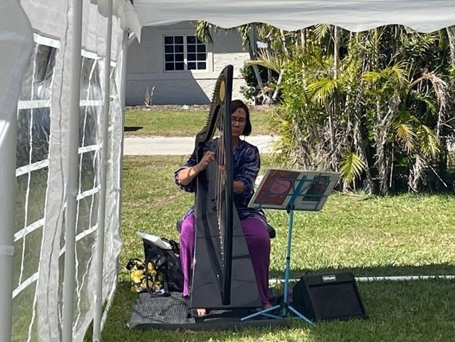 A woman is sitting under a tent playing a harp.