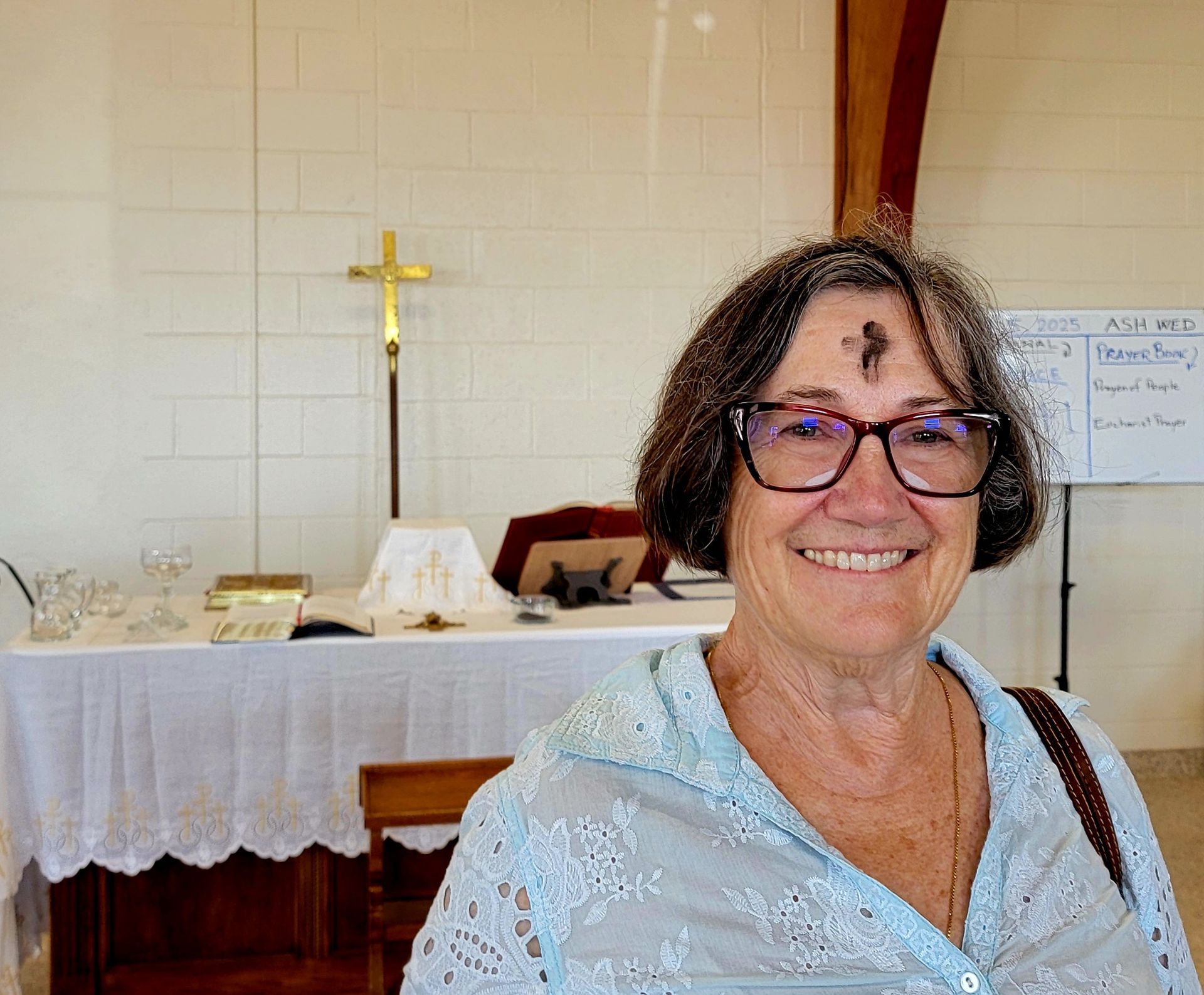 Woman with ash cross on forehead, smiling, standing in a church with a cross and altar behind her.
