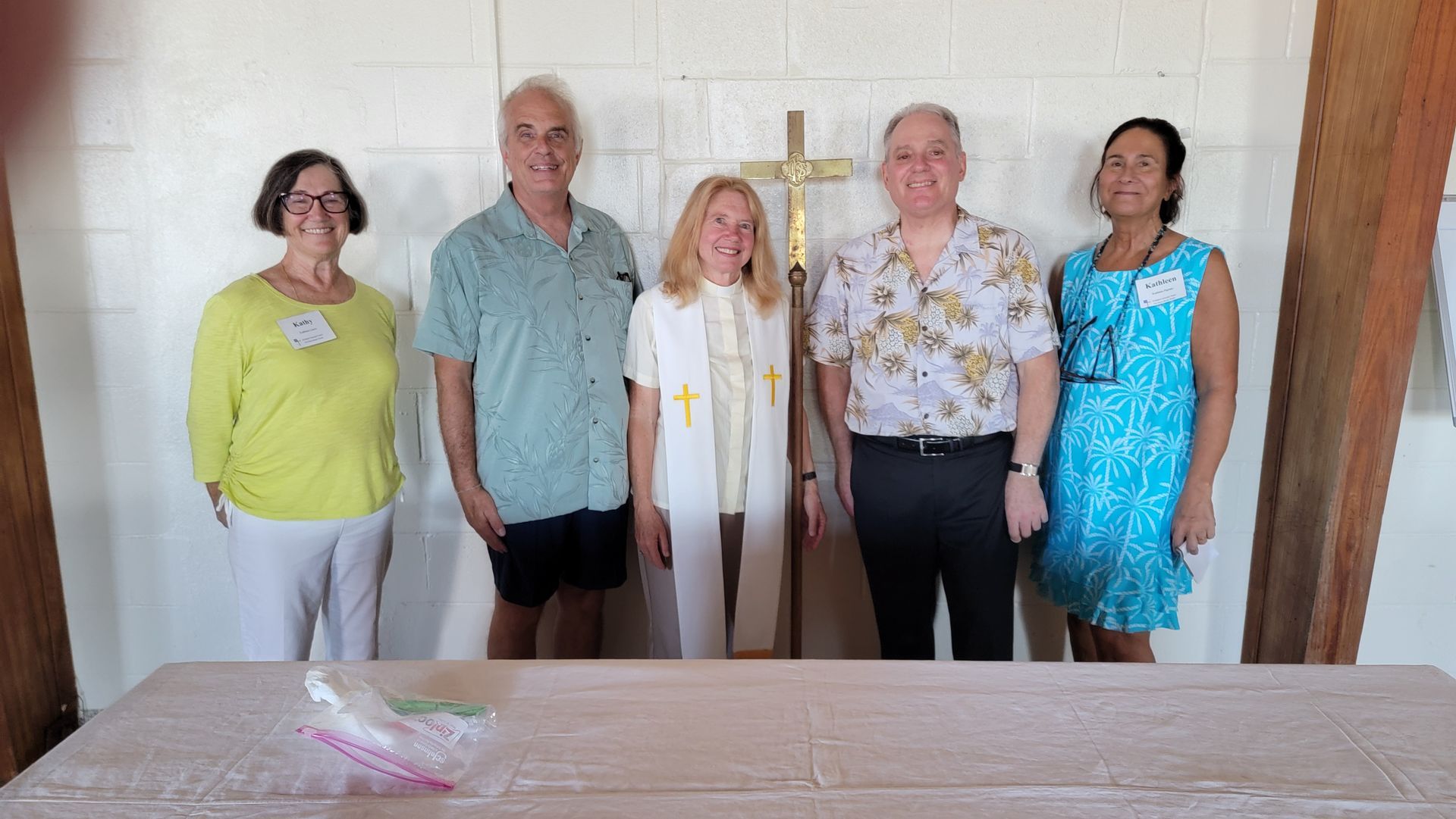Five people standing in front of a cross, smiles. Two women on the left, three men on the right.