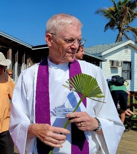 A man in a white robe and purple scarf is holding a plant