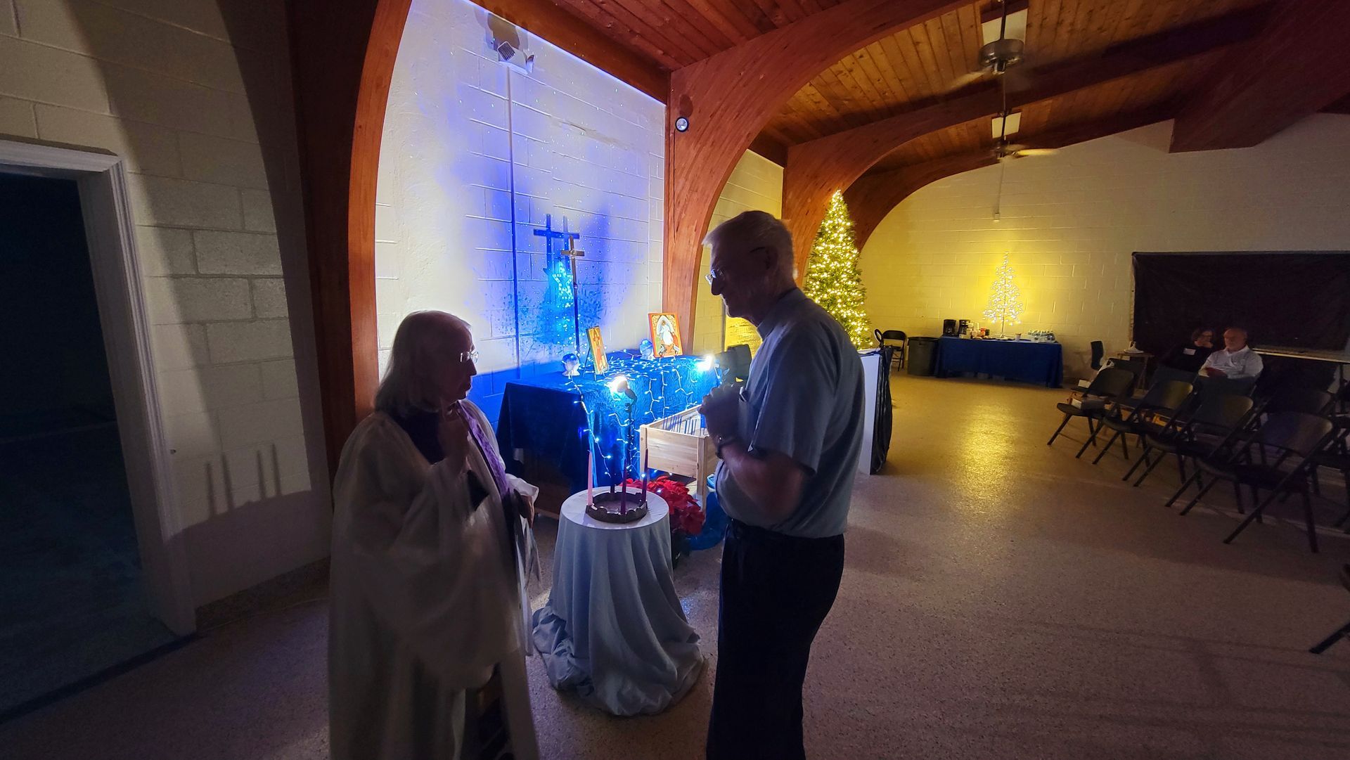 Two people talking near a decorated altar. Christmas decorations, including a tree, in a church.