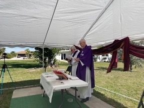A man in a purple robe is standing under a tent reading a book.