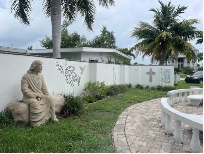 A statue of jesus sitting on a sheep in front of a white wall