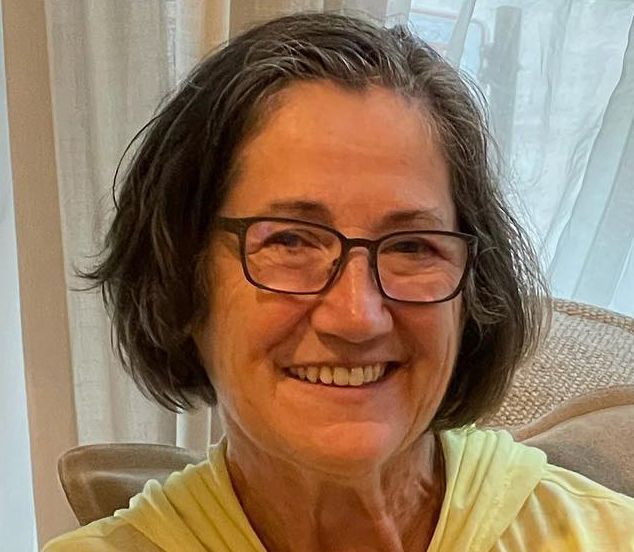 A woman wearing glasses and a yellow shirt is smiling for the camera.