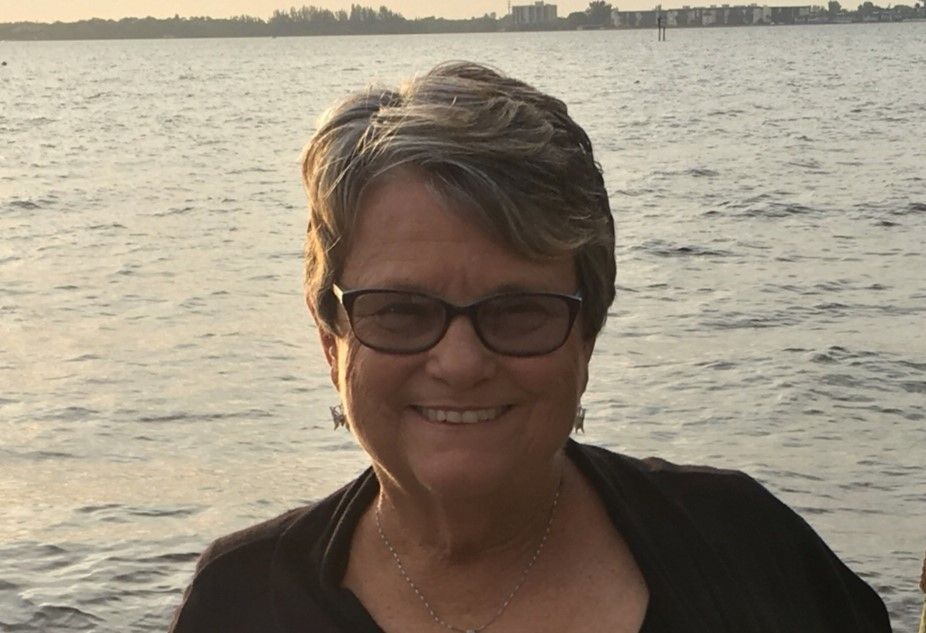 A woman wearing glasses is smiling in front of a body of water.