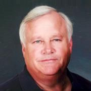 A man with white hair is wearing a black shirt and looking at the camera.