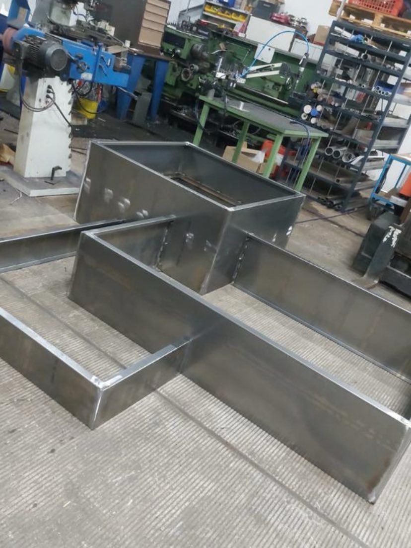 Een metalen frameconstructie, gemaakt van gelaste stalen platen, rust op een betonnen werkplaatsvloer.