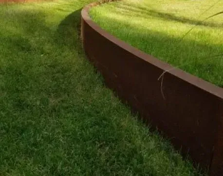 Een gebogen, roestkleurige metalen keermuur scheidt een grasveld van een iets lager gelegen grasveld.