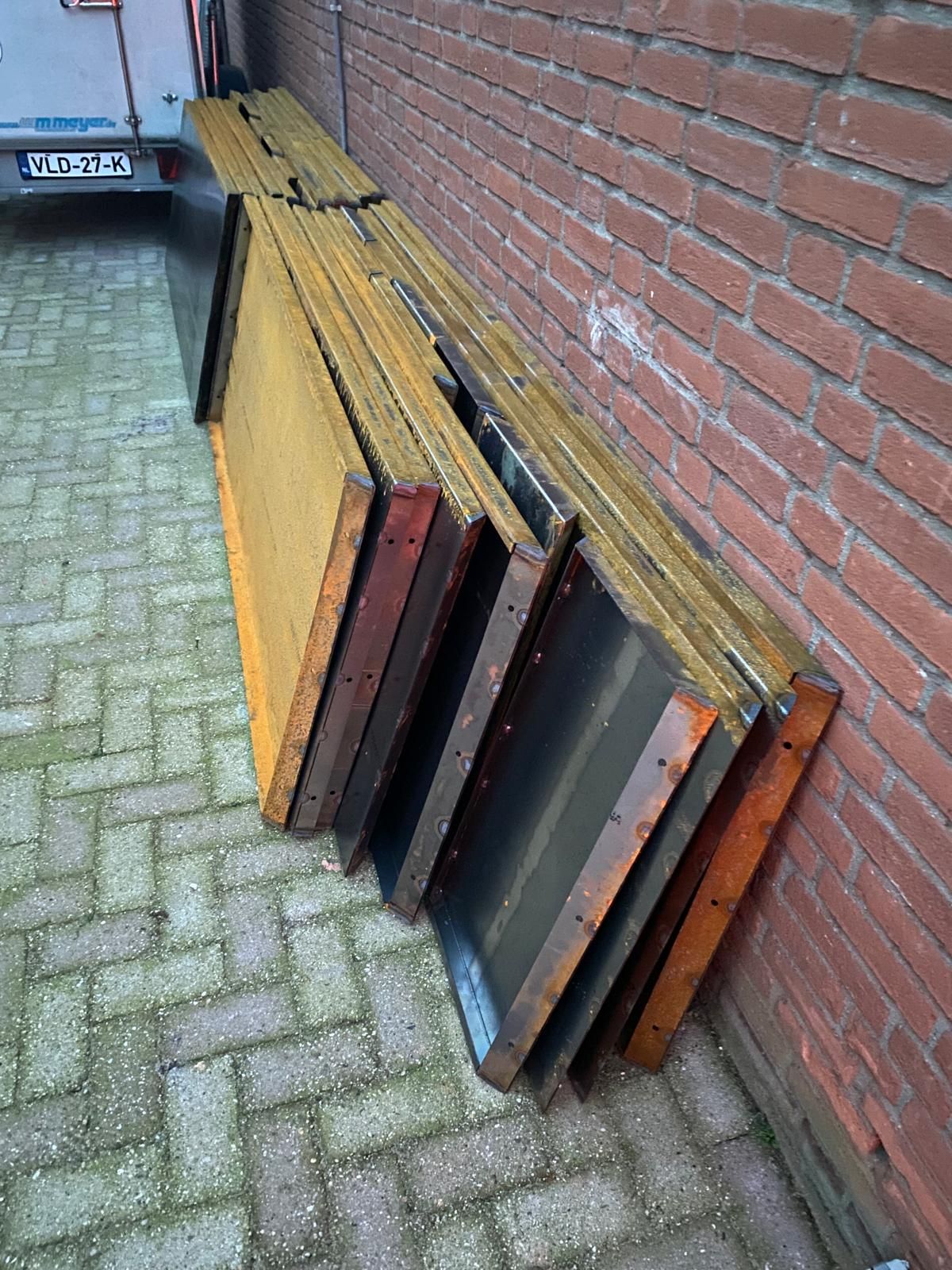 Een rij rechthoekige, geel omlijste betonnen bekistingen leunde tegen een bakstenen muur op een geplaveide ondergrond.