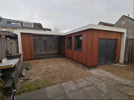 Moderne L-vormige aanbouw in de achtertuin met houten lambrisering, grote glazen schuifdeuren en donkergrijze dubbele deuren.