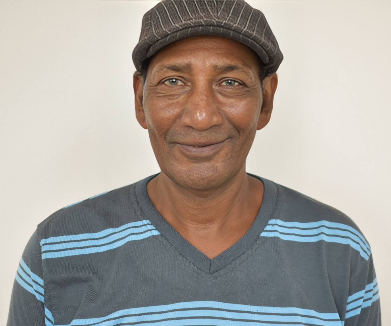 A man wearing a hat and a striped shirt smiles for the camera
