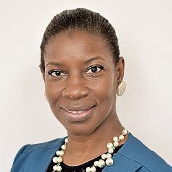 A woman wearing a blue jacket and a pearl necklace is smiling for the camera.