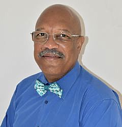 A bald man with glasses and a mustache is wearing a blue shirt and a bow tie.