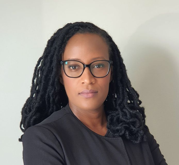 A woman with dreadlocks is wearing glasses and a black jacket.