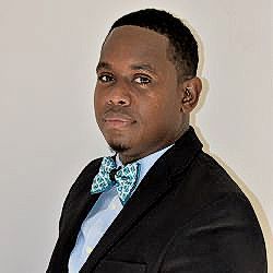 A man in a suit and bow tie is standing in front of a white wall.