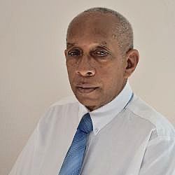 A man in a white shirt and blue tie is looking at the camera.
