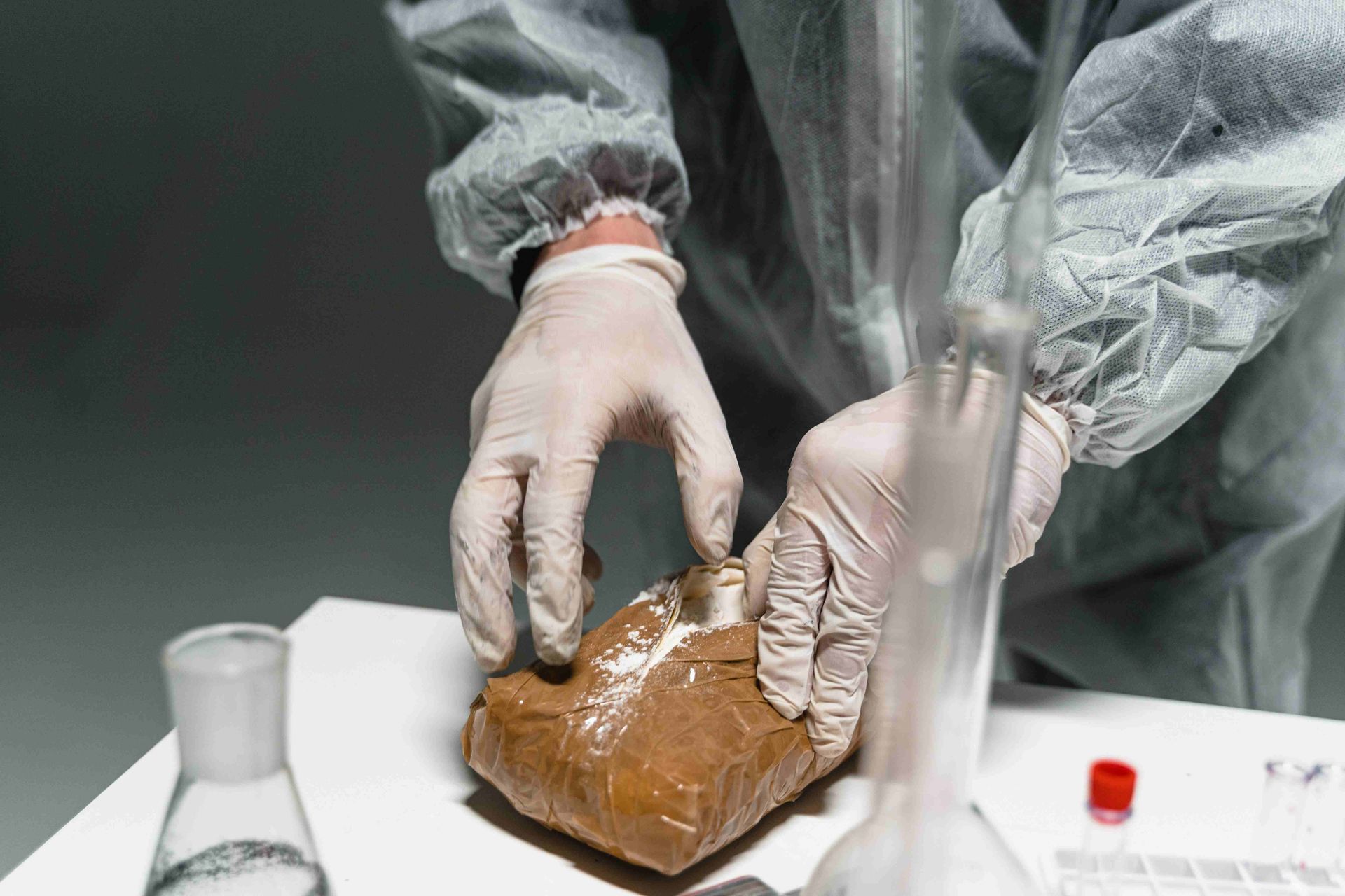 A person wearing gloves is holding a bag of brown powder.