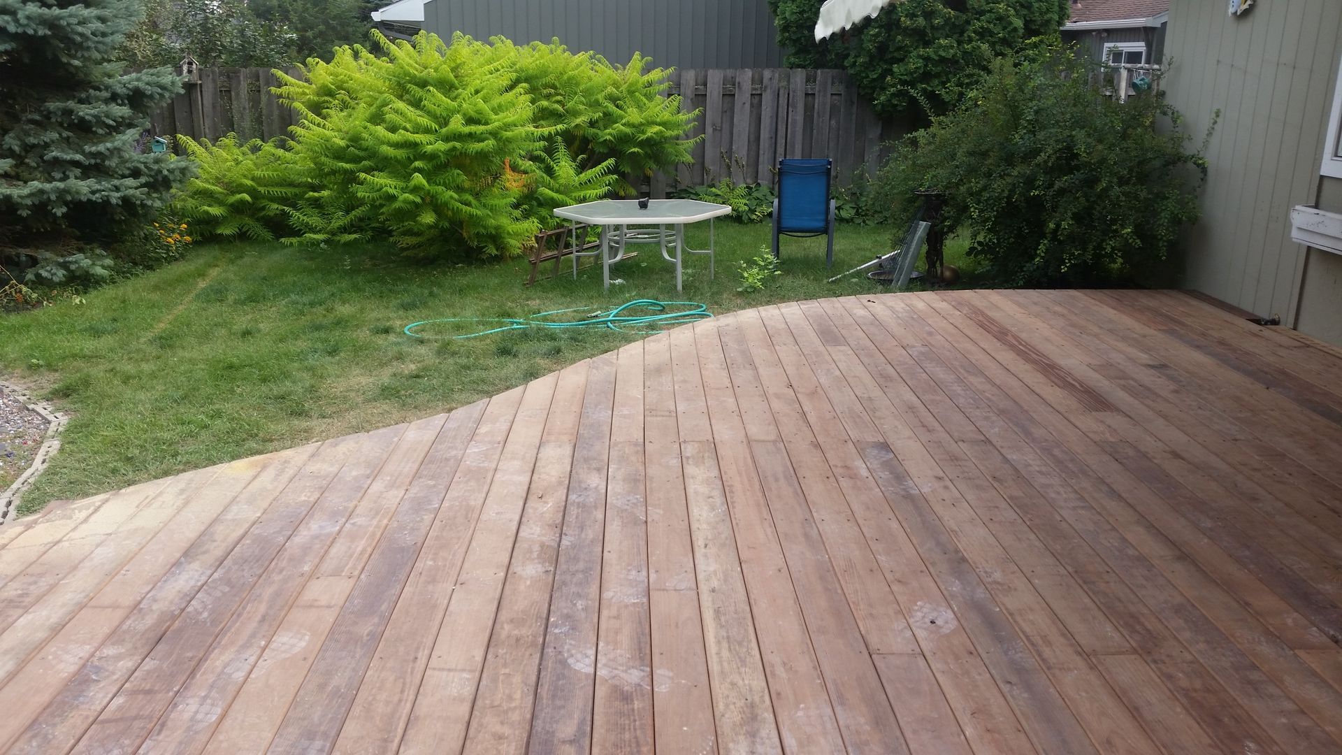 A wooden deck in a backyard with a table and chairs.