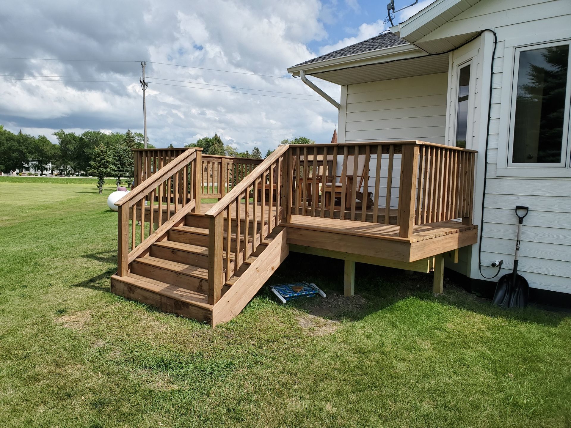 A wooden deck with stairs leading up to it is in front of a white house.