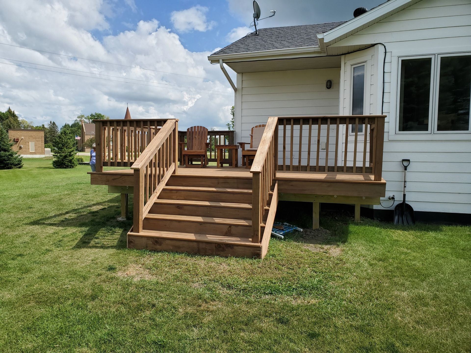 A wooden deck with stairs leading up to it is in front of a white house.
