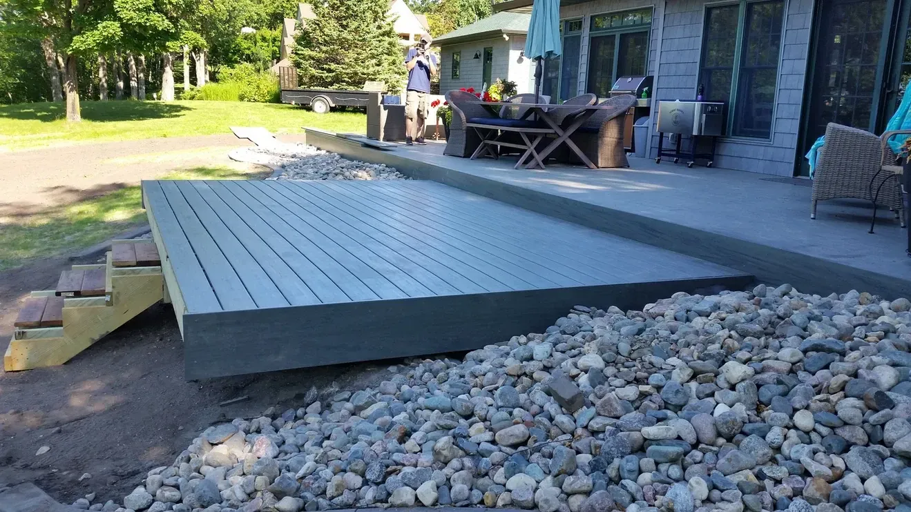 A wooden deck is sitting on top of a pile of rocks in front of a house.