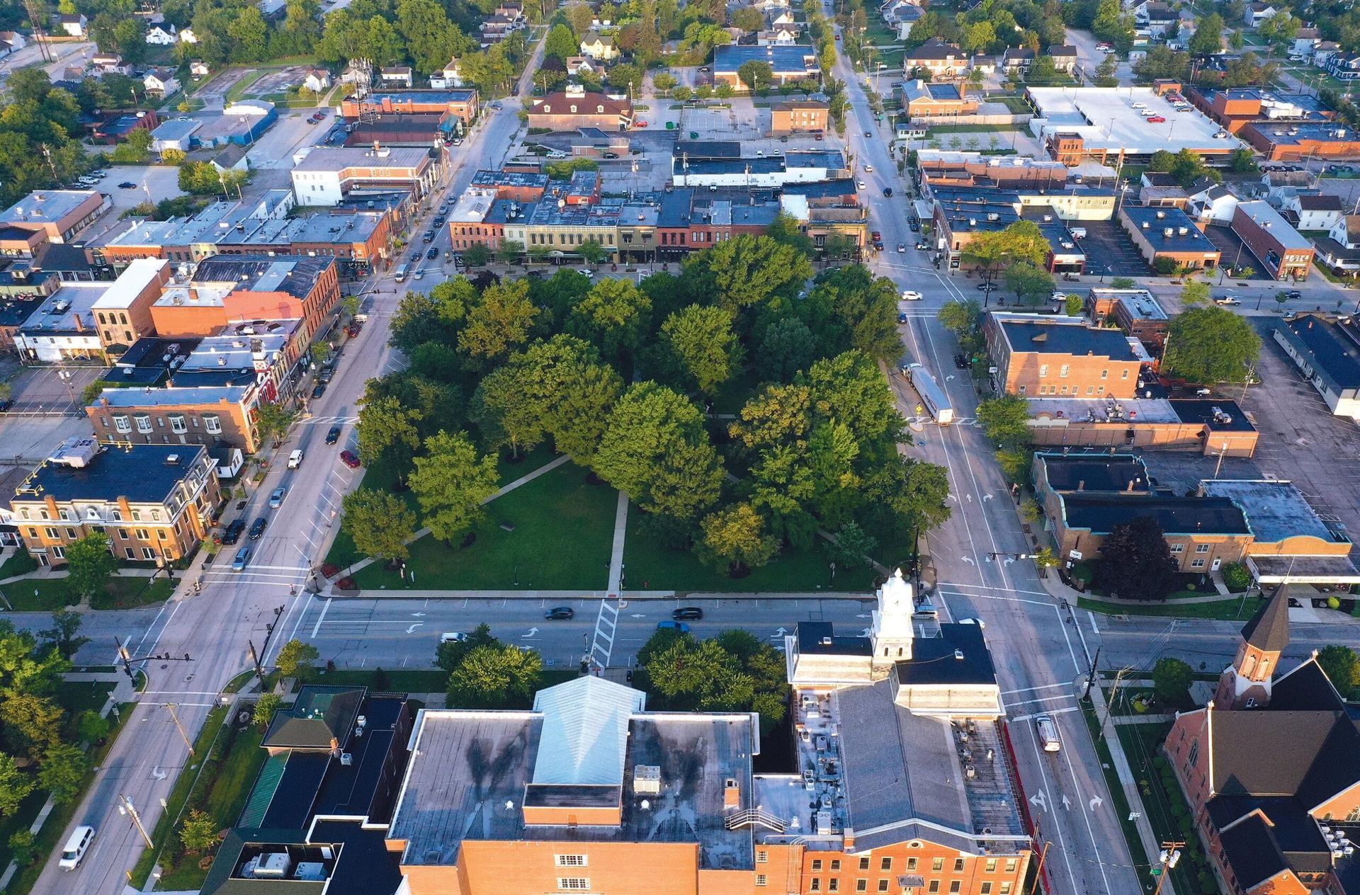 Aerial view of a city park with trees, surrounded by streets and brick buildings at sunset