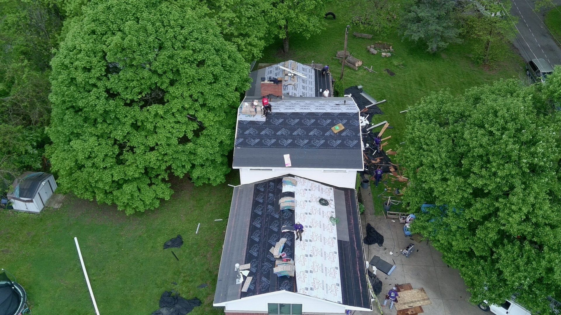 Aerial view of a white house with a dark roof surrounded by dense green trees and lawn