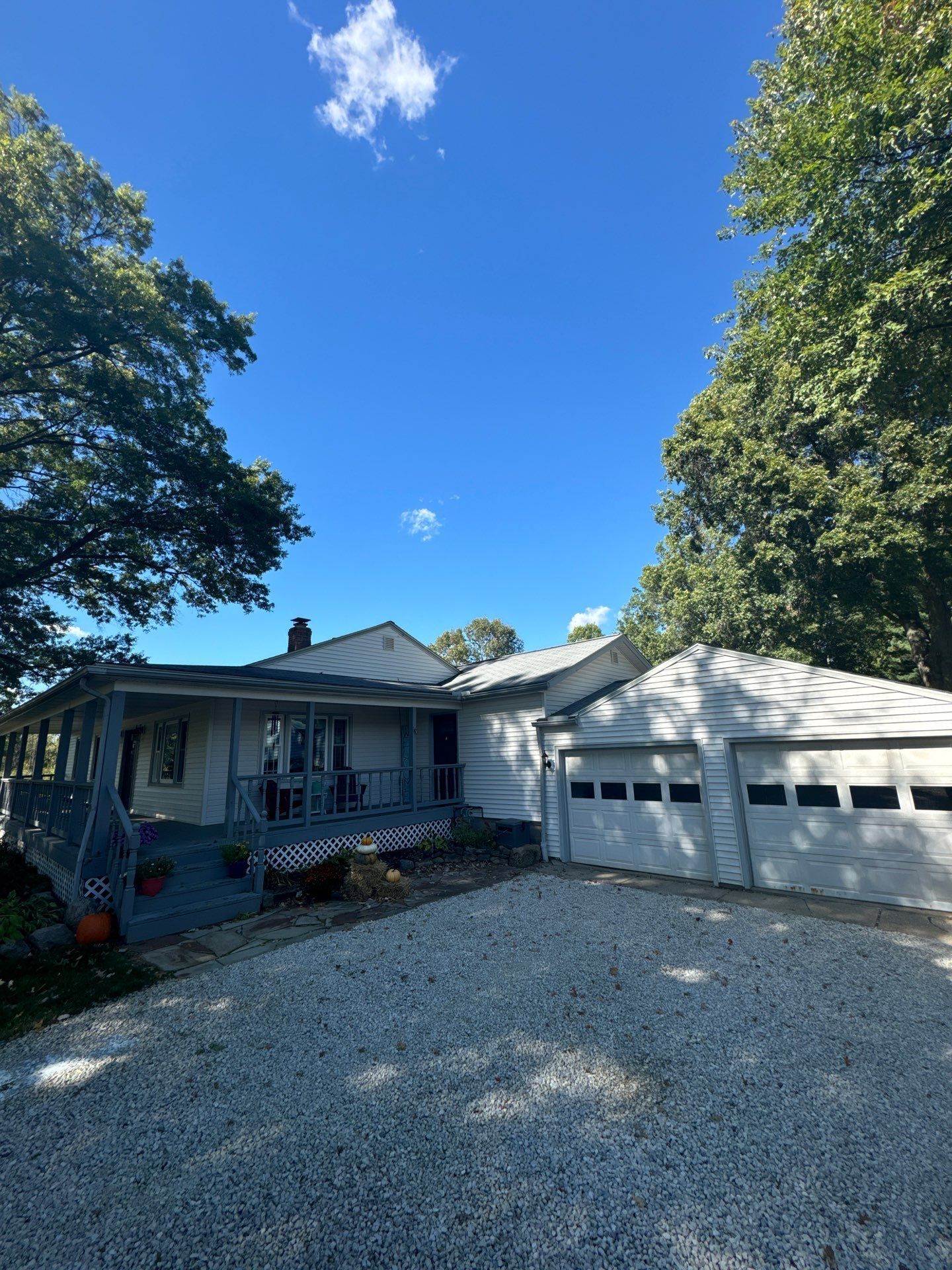 Single-story house with a white garage, gravel driveway, and trees under a bright blue sky