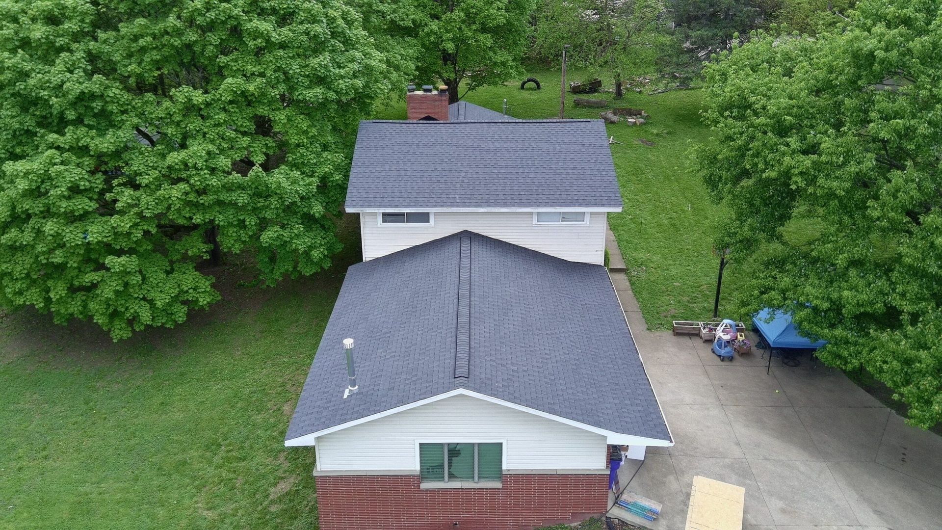 Aerial view of two houses with gray roofs, surrounded by green trees and a driveway.
