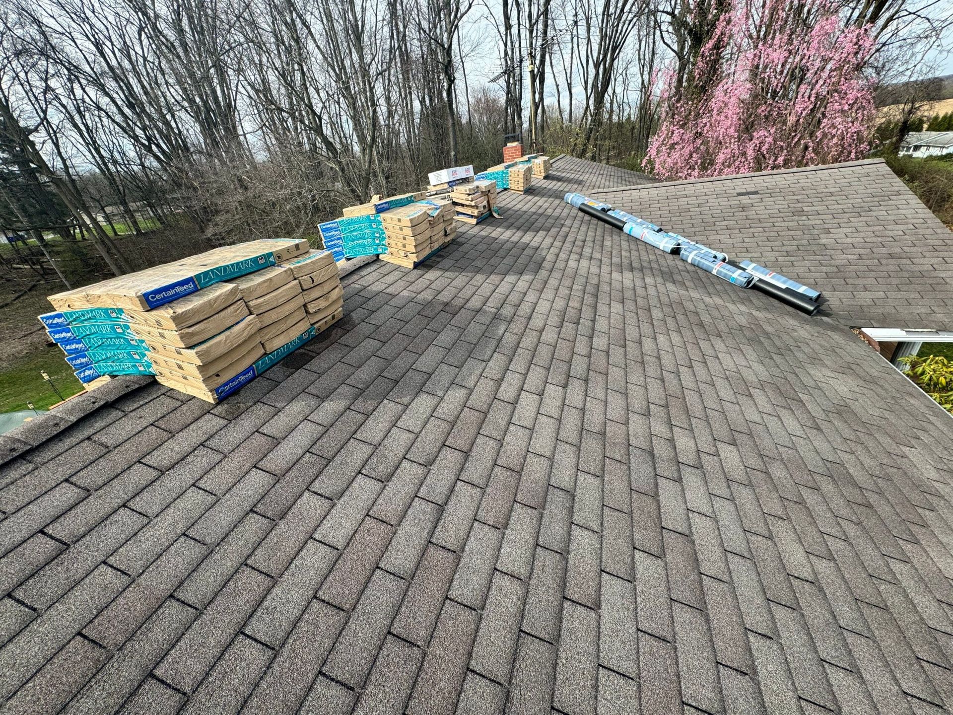 Stacked bricks and supplies lined along a sloped rooftop, with trees and pink blossoms in the background.