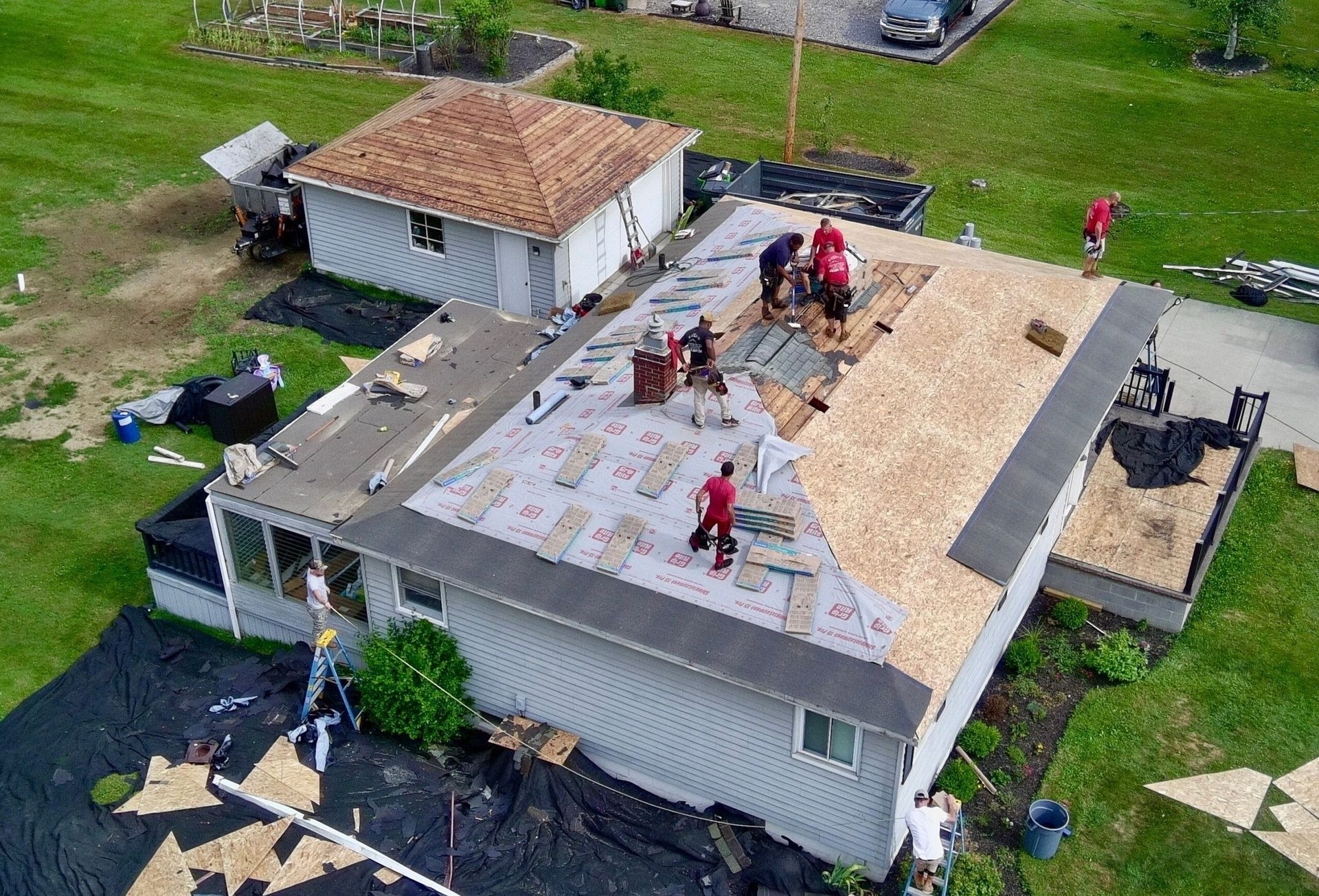 Workers installing a roof on a white house with shingles removed and materials spread across the roof.