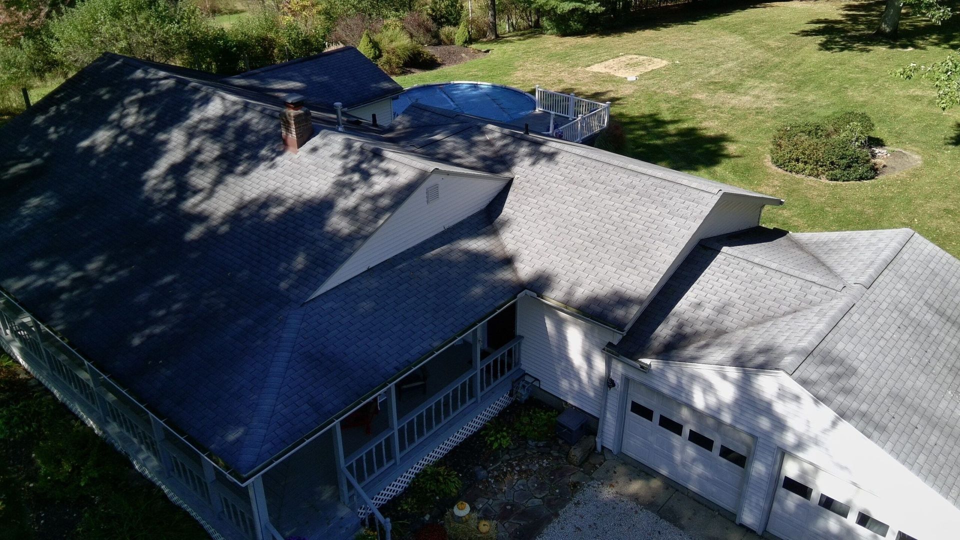 Aerial view of a house with a dark roof, white siding, and a grassy yard around it.