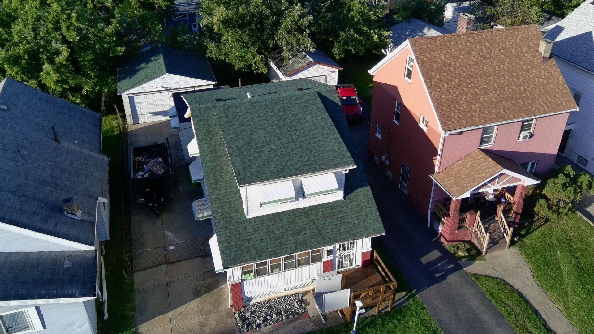 Aerial view of three suburban houses with driveways, lawns, and a parked car between them.