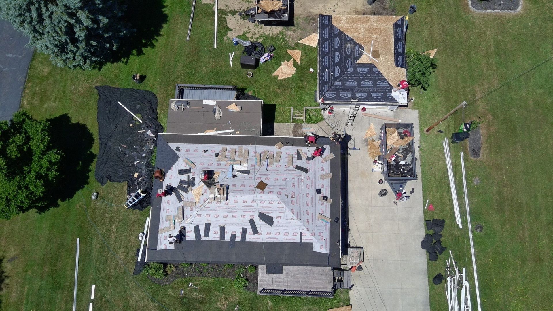 Aerial view of a house roof under repair, with workers, tools, and scattered roofing materials.